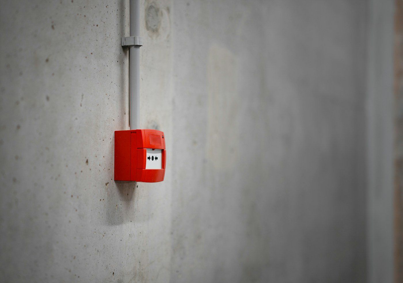 Red fire alarm manual call point on a concrete wall
